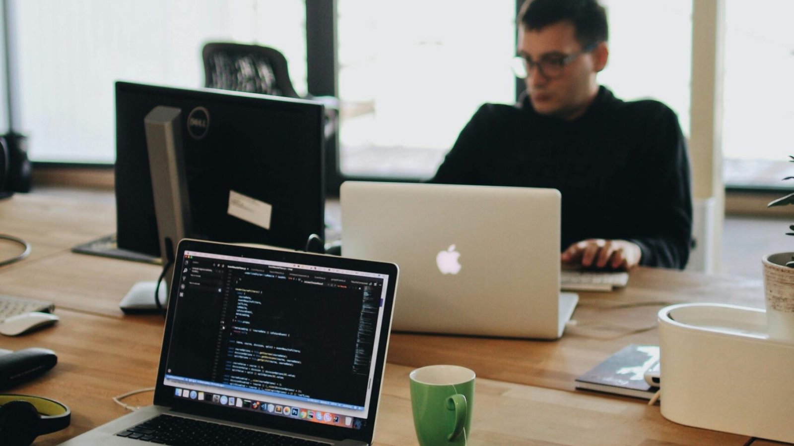 A web developer working on code in a modern office setting with multiple devices.